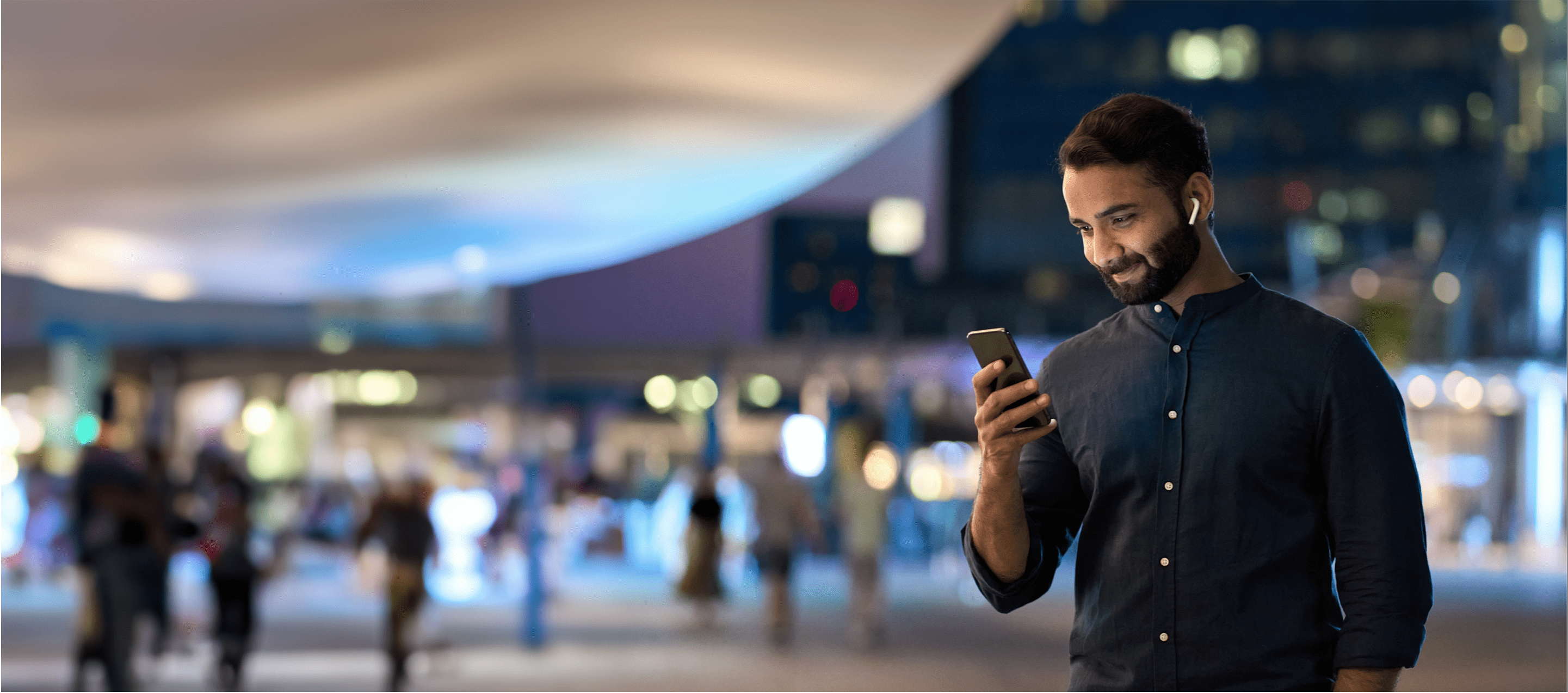 A businessman checking his mobile phone whilst standing outdoors in a city at night time