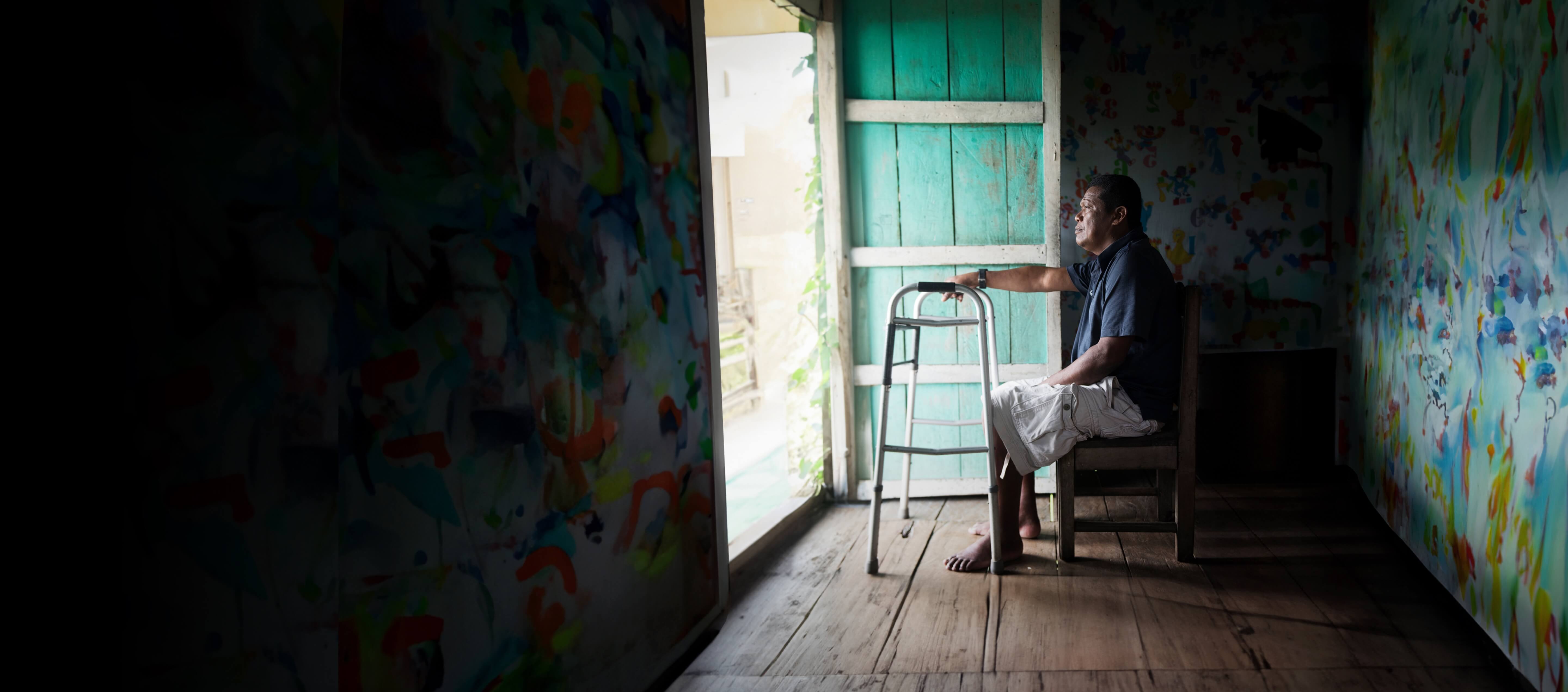 A senior gentleman sat down with his walking frame infront of him