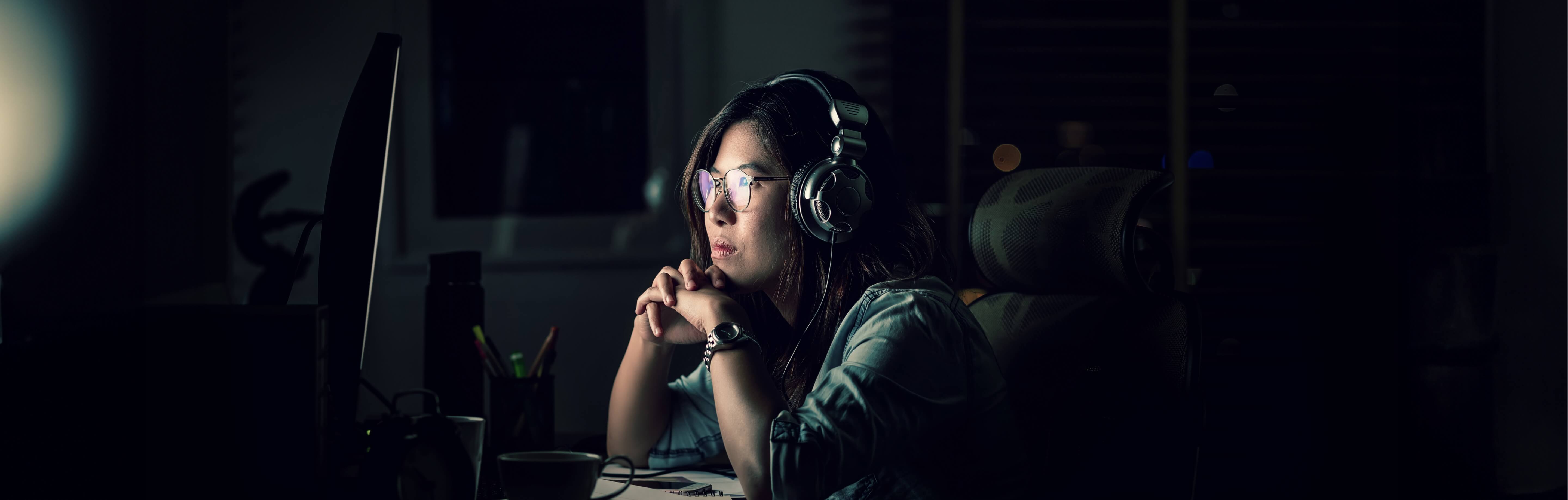 A young female graduate sat in darkeness while working at a computer